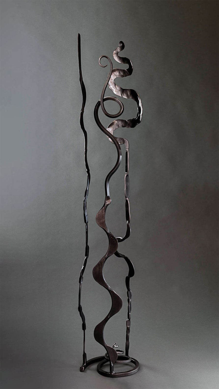 A metallic black abstract sculpture that has a spiral base and three different shaped elements rising from it.