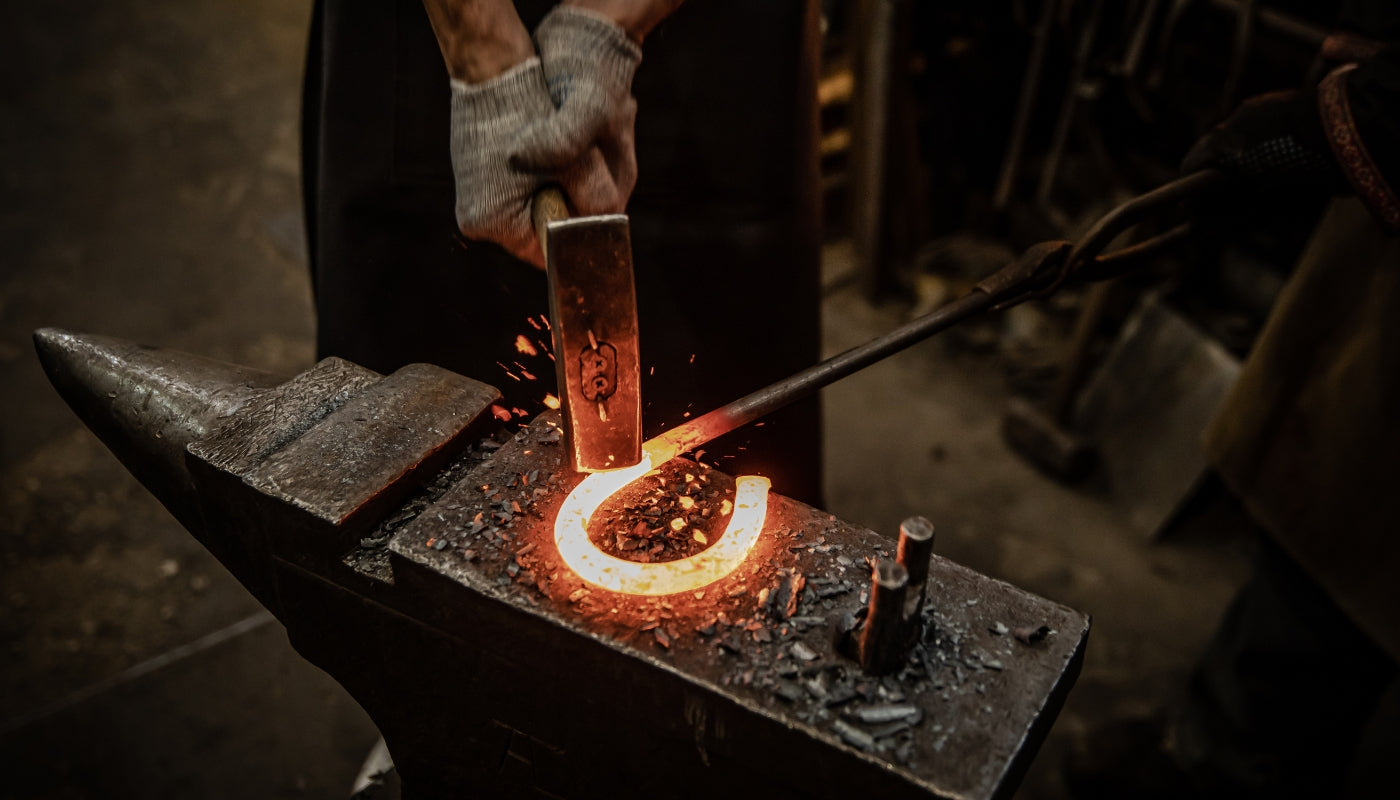 Top down view of a blacksmith hammering a red hot piece of steel at the anvil.