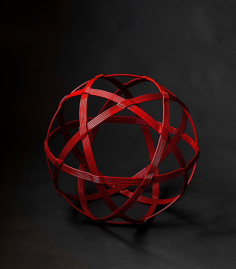 Red metal garden sphere sculpture shaped like a Chinlone wicker ball.