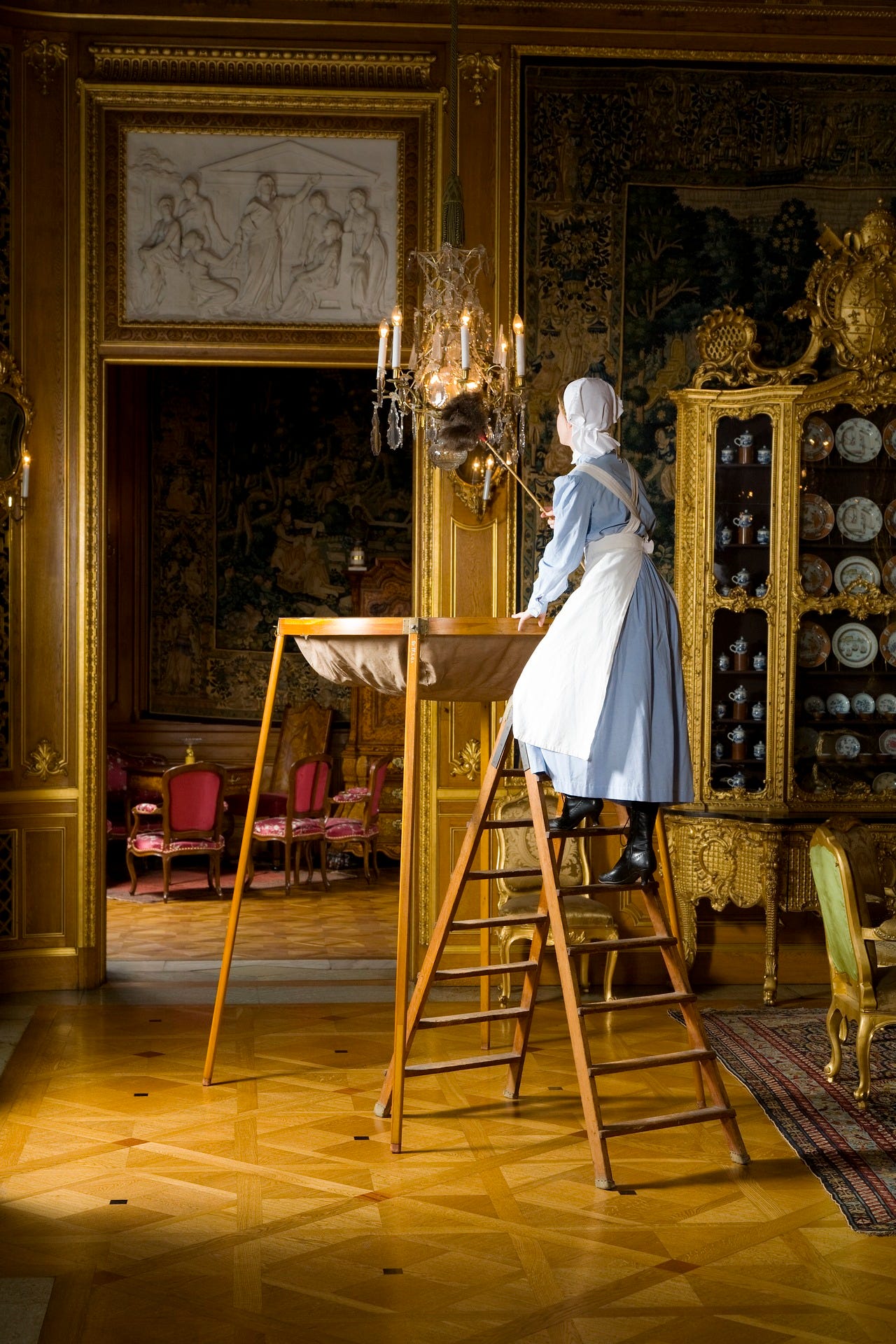 Woman lighting a candle chandelier in a renaissance style scene.