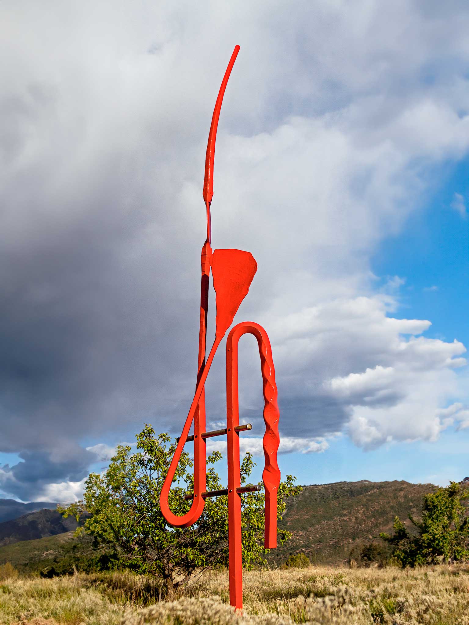 12 foot tall red, abstract sculpture made of steel standing alone in a high desert landscape.