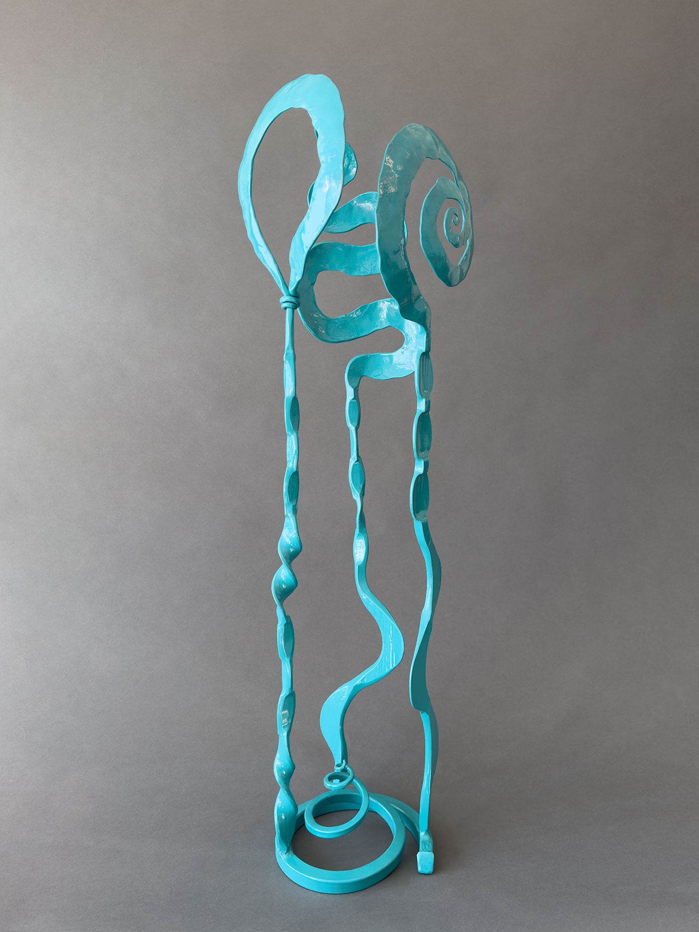 Small turquoise metal garden sculpture made of hand forged steel. Sculpture has a spiral base and three individual standing elements with abstract designs.