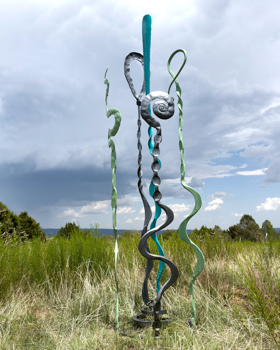 Metal sculpture with wavy designs in a grassy field under a cloudy sky
