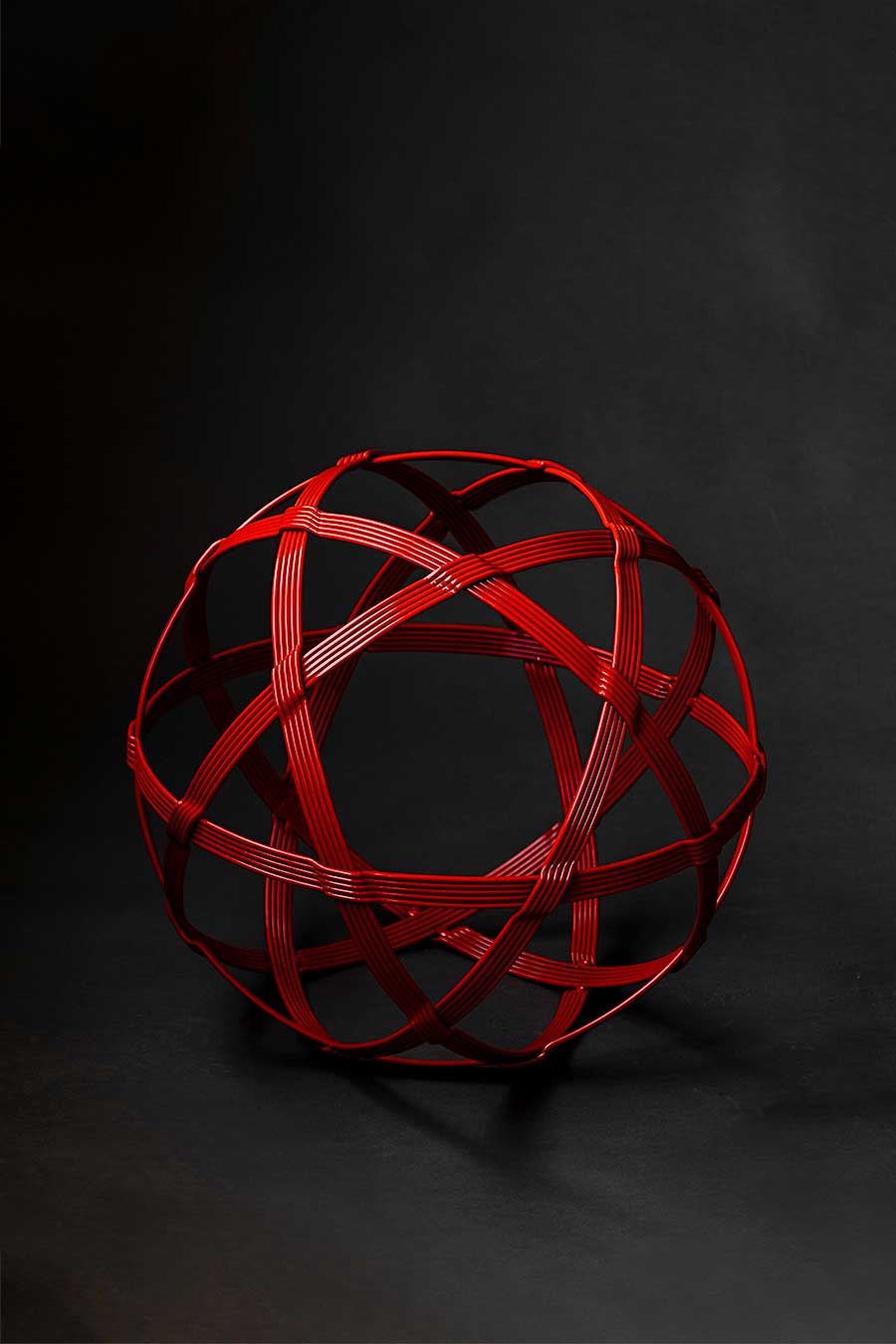 A 19 inch round red steel orb sculpture resembling a chinlone wicker ball, hand-forged by New Mexico blacksmith Christopher Thomson.