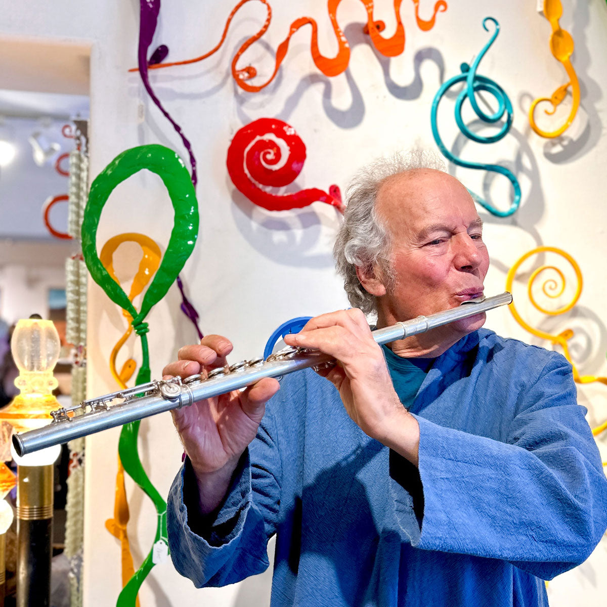 Man playing a flute in front of colorful musical instrument decorations
