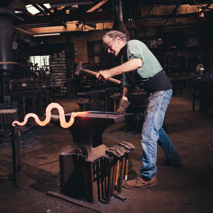 Steel sculpture artist, Christopher Thomson, hammering at the anvil.