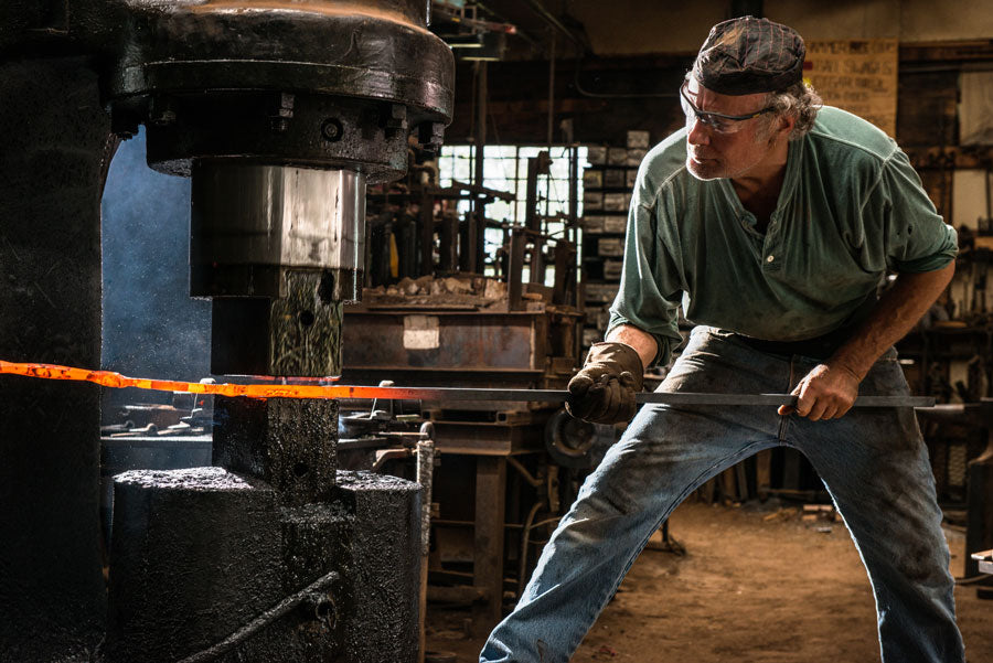 Blacksmith using a power hammer in his blacksmith shop.