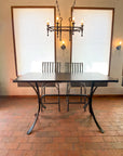 Wrought iron martini bar table with two forged bar stools on a brick floor, under an iron candle chandelier