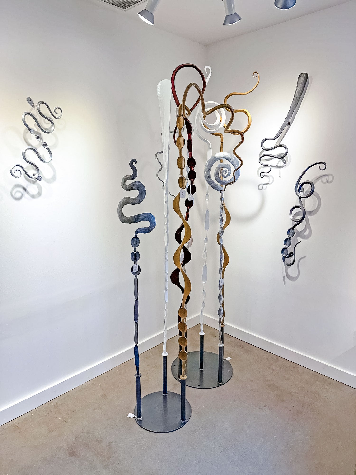 Artistic metal sculptures on stands against a white wall in an exhibition setting.