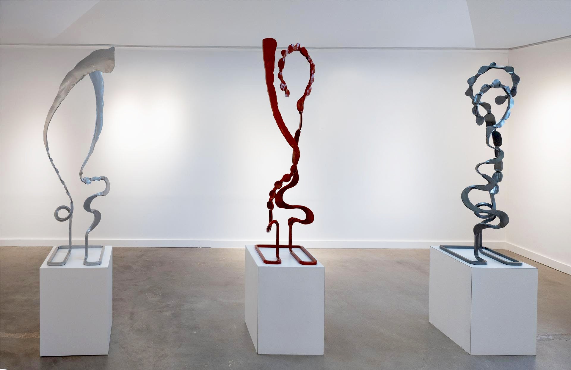 Three abstract sculptures by Christopher Thomson on white plinths against a white wall.