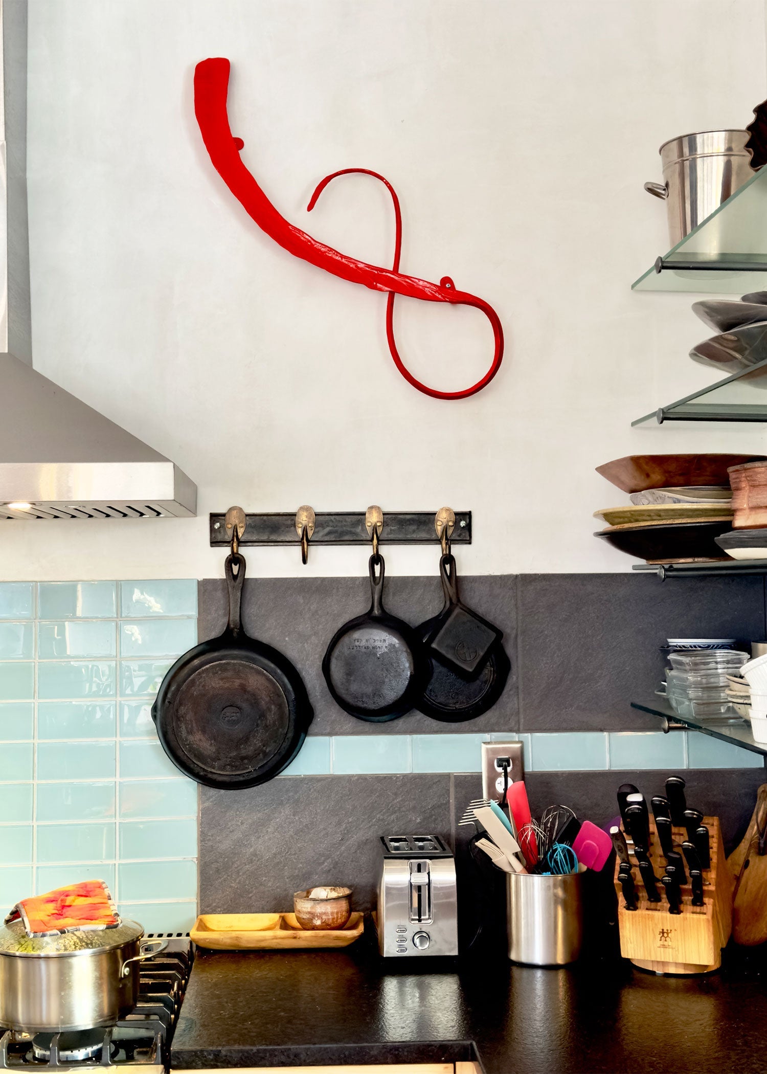 Kitchen counter scene with a red abstract metal wall sculpture.