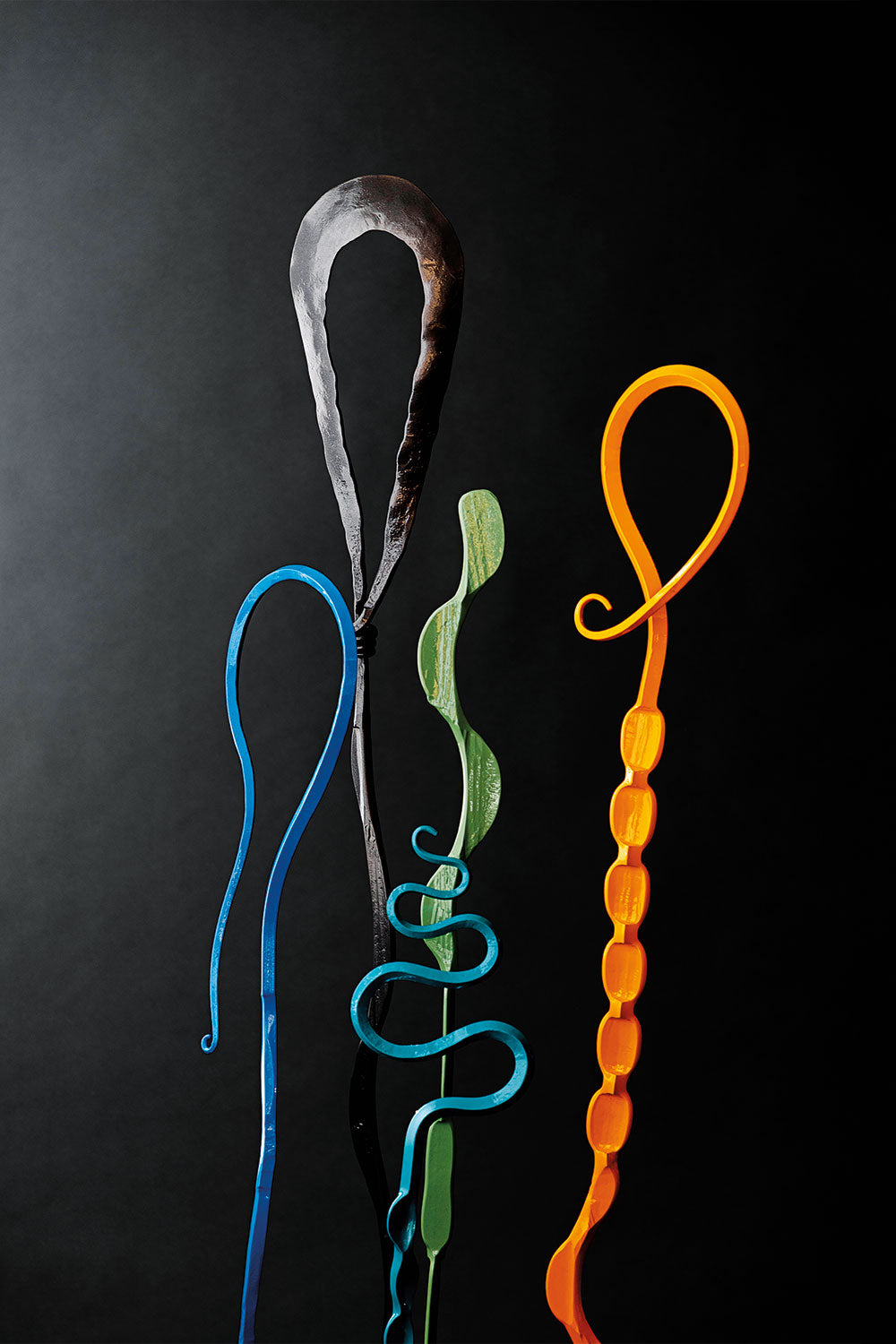Five different abstract shaped steel sculptures in the colors blue, black, turquoise, green and yellow. These Single Blooms were handmade by blacksmith, Christopher Thomson Ironworks.