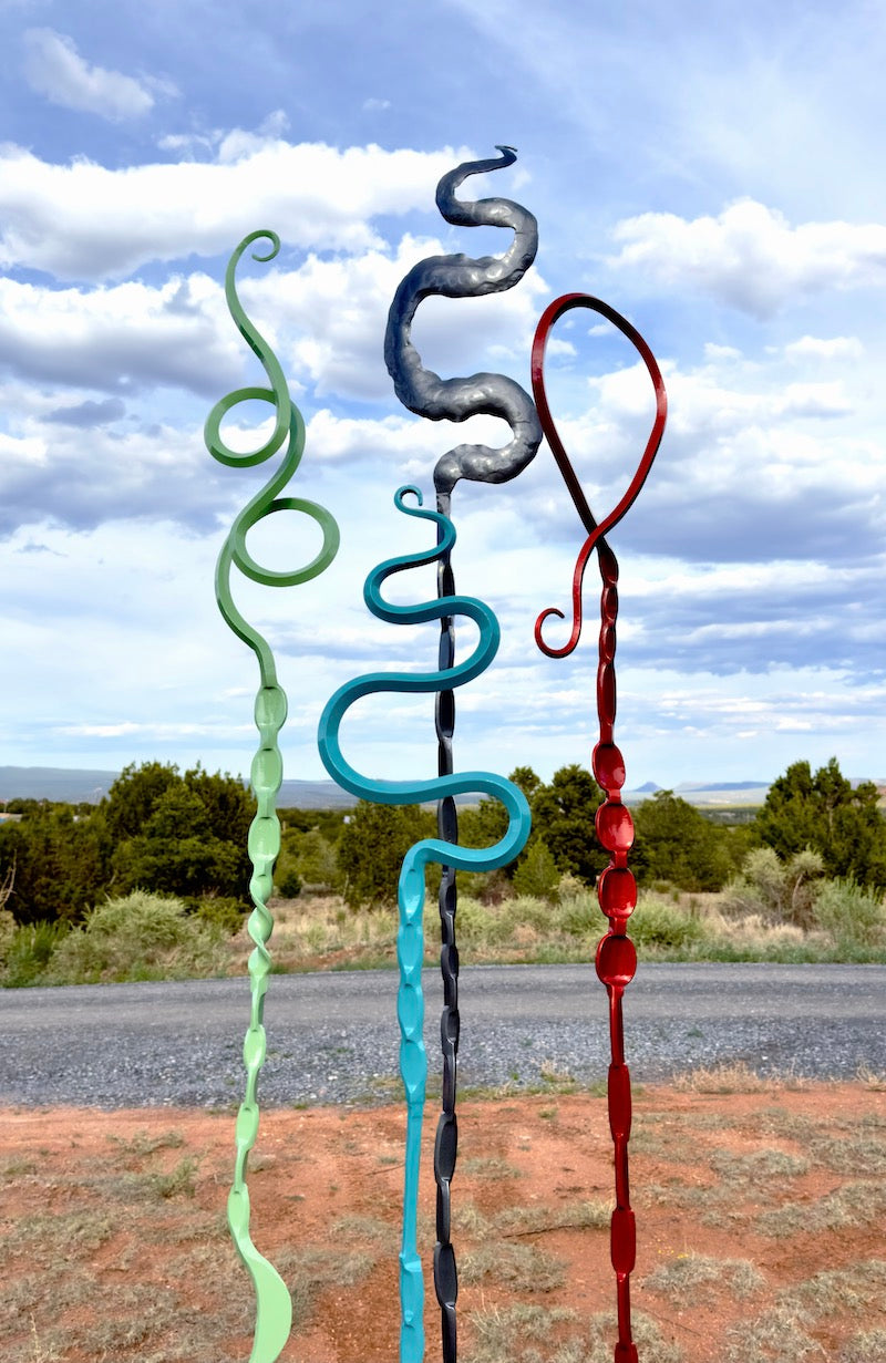 Colorful abstract steel sculptures on a road with a scenic background.