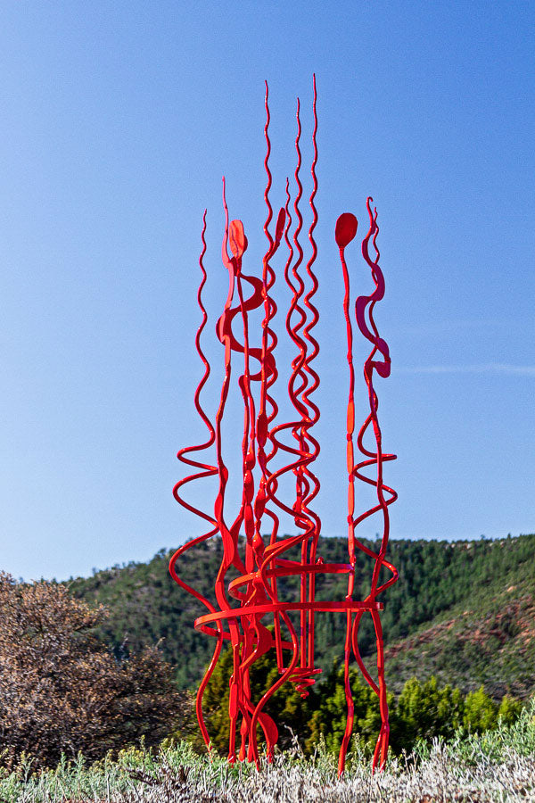 A large abstract, red sculpture standing in a mountainous landscape. Hand forged by artist / blacksmith Christopher Thomson Ironworks.