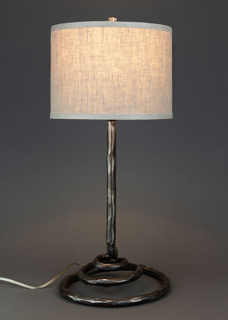 High end wrought iron lamp with a spiral base shown with a linen drum shade. Lamp made by blacksmith Christopher Thomson in New Mexico.