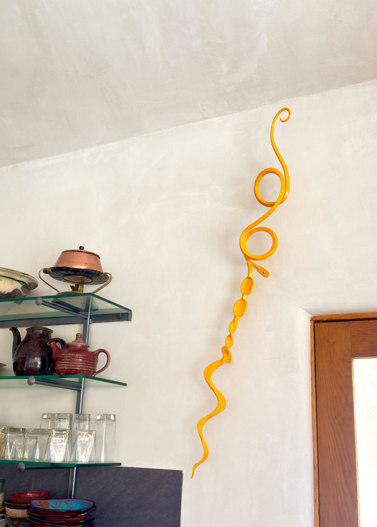 Abstract yellow metal wall sculpture hanging on the wall by a doorway.