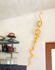 Abstract yellow metal wall sculpture hanging on the wall by a doorway.