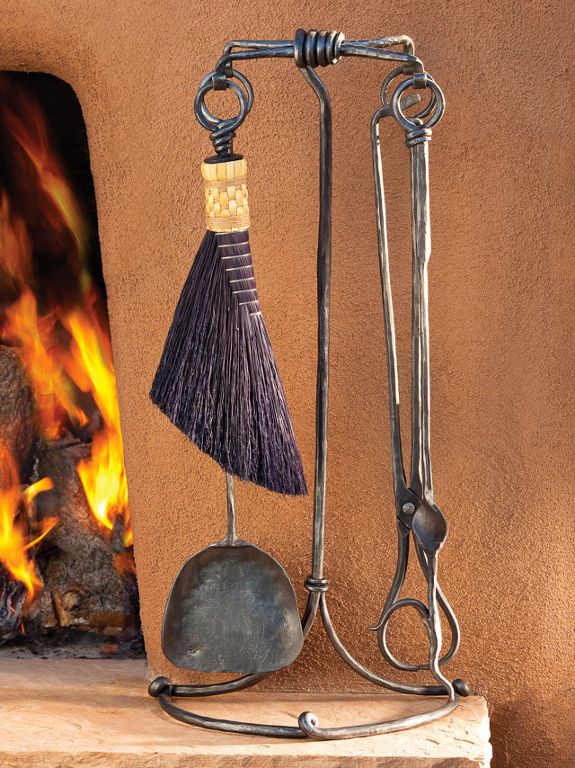 Wrought iron forged fireplace tool set standing next to a kiva fireplace.