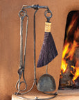 Wrought iron fireplace tool set with heavy duty stand sitting next to a kiva fireplace.