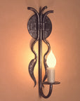Hand-forged wrought iron candle wall sconce with two chili-shaped accents hanging from the backplate, featuring a candle-shaped bulb, in a rustic Southwestern style.