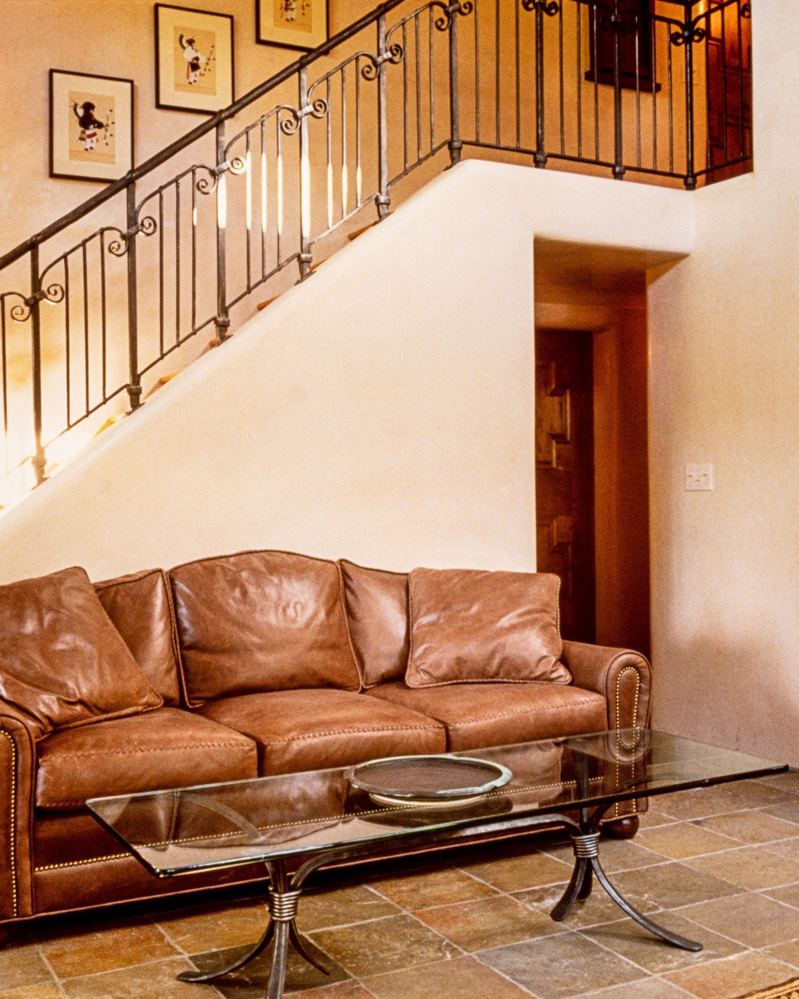 A sitting area with a wrought iron coffee table and a brown leather couch positioned just in front of a staircase with a custom wrought iron staircase railing.