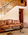 A sitting area with a wrought iron coffee table and a brown leather couch positioned just in front of a staircase with a custom wrought iron staircase railing.