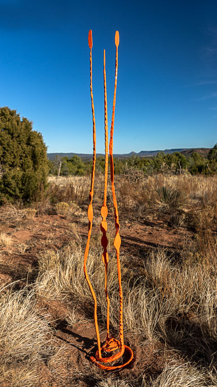 Orange forged steel Pajo sculpture with three vertical pieces of steel affixed to a spiral base.