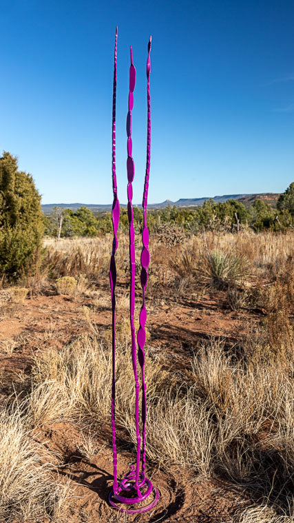 Purple metal steel sculpture with a small spiral base and three tall tendrils coming up from the base.