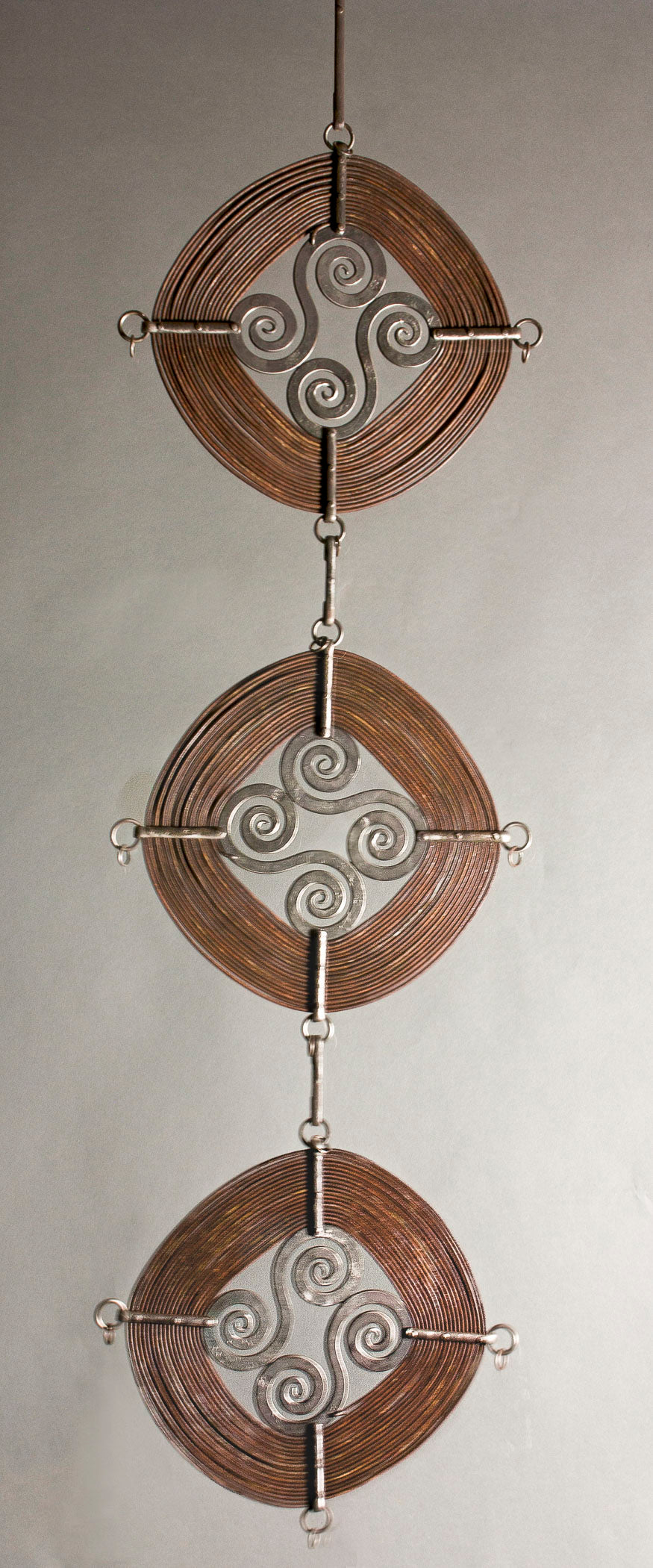Three "Windings" sculptures hanging off each other forming a vertical column.