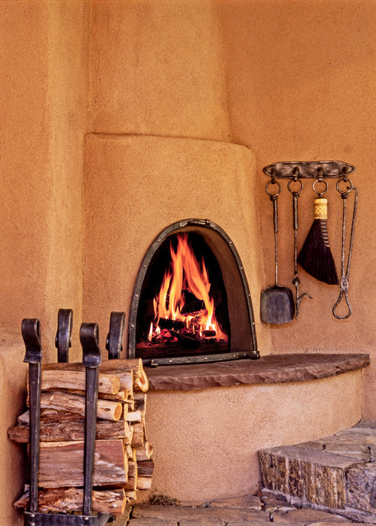 Outdoor fireplace with wrought iron fireplace tools showing a log holder, fireplace screen and a wall mounted fireplace tool set hanging by the fireplace.
