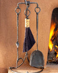 Heavy duty outdoor wrought iron fireplace tools with a broom, shovel and a poker standing next to a kiva fireplace.