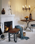 Living room furnished with luxury wrought iron furnishings by Christopher Thomson Ironworks featuring a fireplace tool set, bench, hanging chandelier, table and chair.