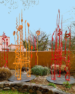Red and Orange hand forged spiral sculptures by Christopher Thomson on display in a garden. 