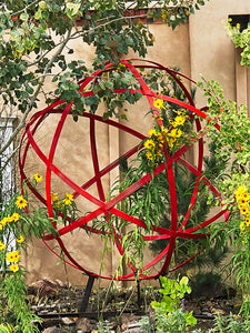 A steel red chinlone orb sculpture by artist blacksmith, Christopher Thomson on display in a courtyard in Santa Fe, New Mexico.