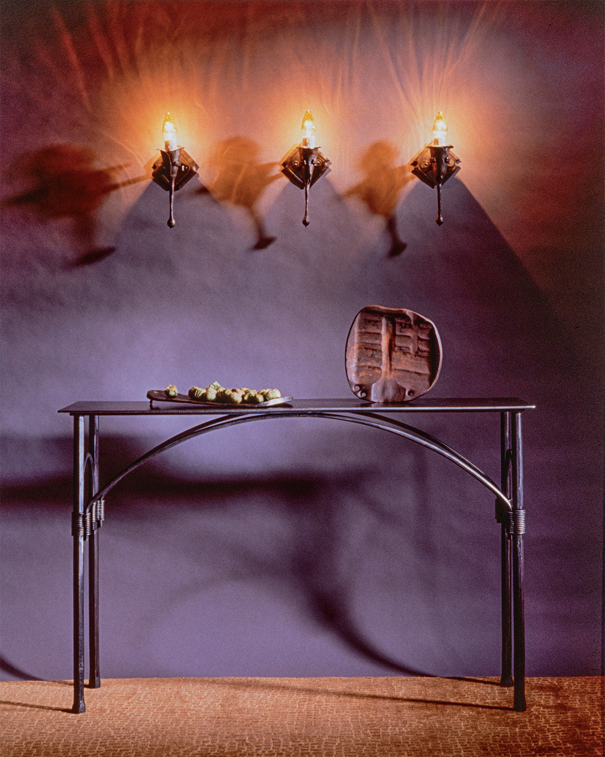 Wrought iron console table with an arched design underneath the table top. Hand forged table sits beneath three wrought iron light fixtures.