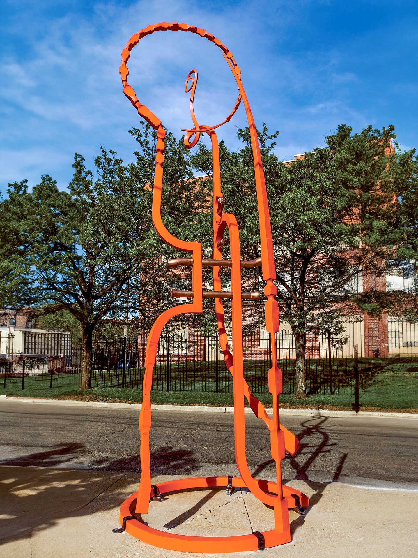 A very large orange colored steel sculpture that stands on a sidewalk in town.