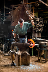 Christopher Thomson in his blacksmith shop forging and hammering a steel sculpture.