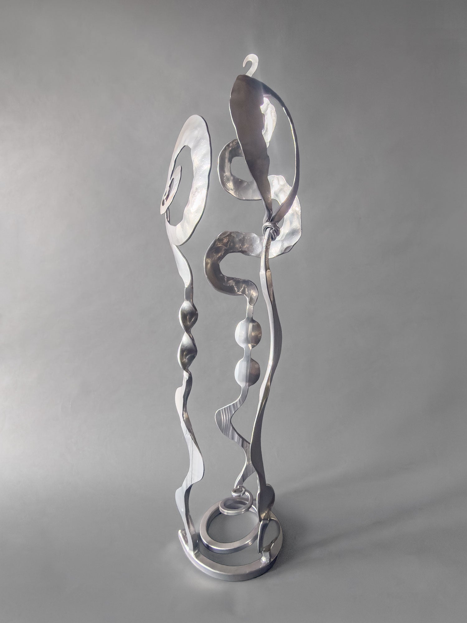 Side view of Chrome Baby Bloom steel sculpture showing Meander form winding through the stem and spiral base