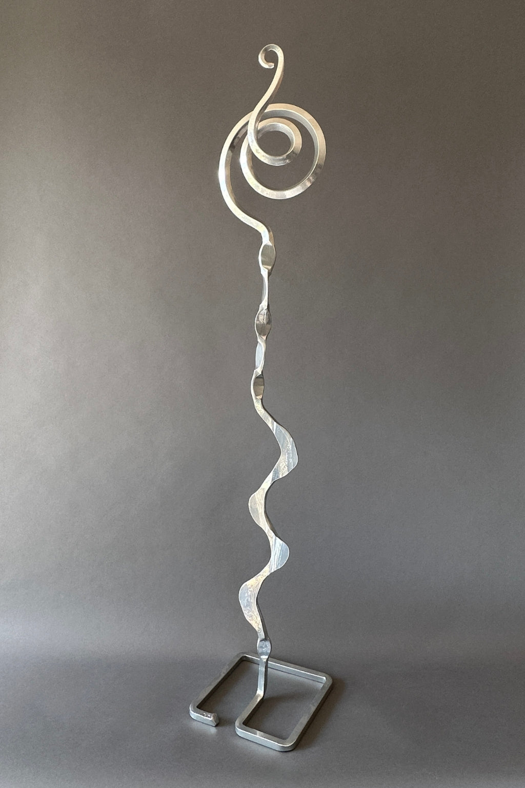 Chrome steel sculpture with a spiral design on a gray background