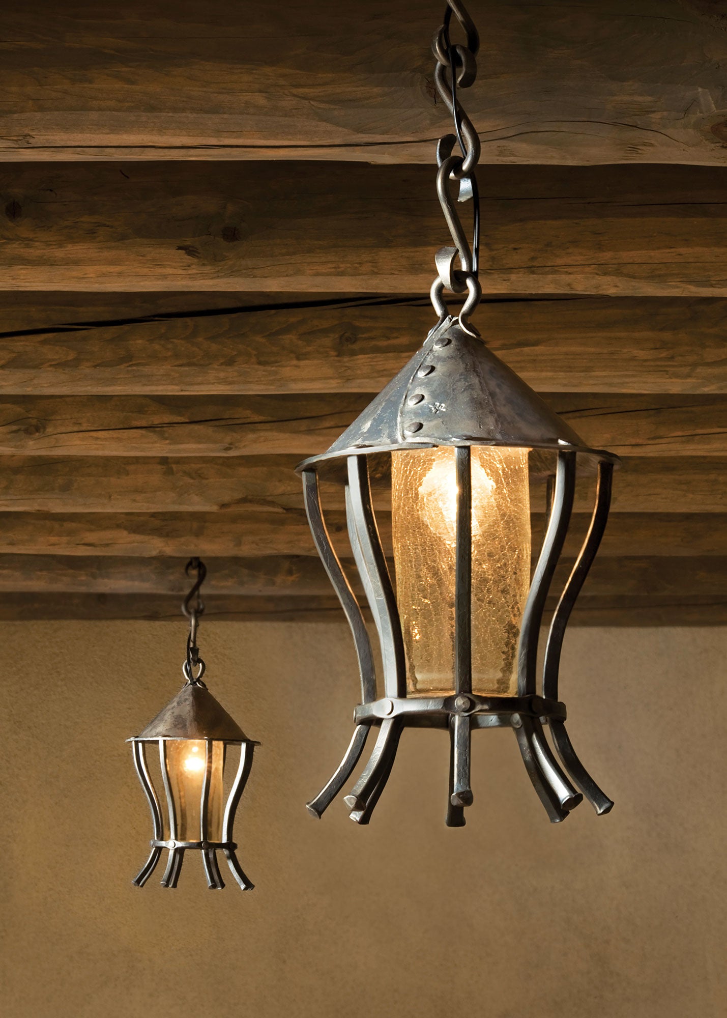 Two hanging lantern-style lights with a rustic design against an adobe wall.