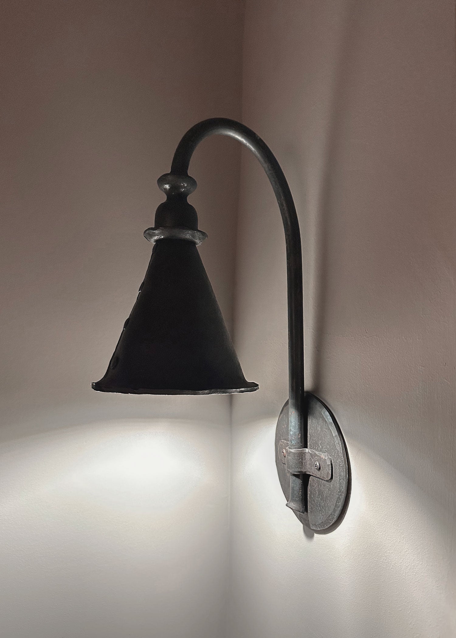 Side view of Entry Wrought Iron Wall Sconce showing a round hand forged backplate illuminated by the cone shaped shade.