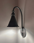 Side view of Entry Wrought Iron Wall Sconce showing a round hand forged backplate illuminated by the cone shaped shade.
