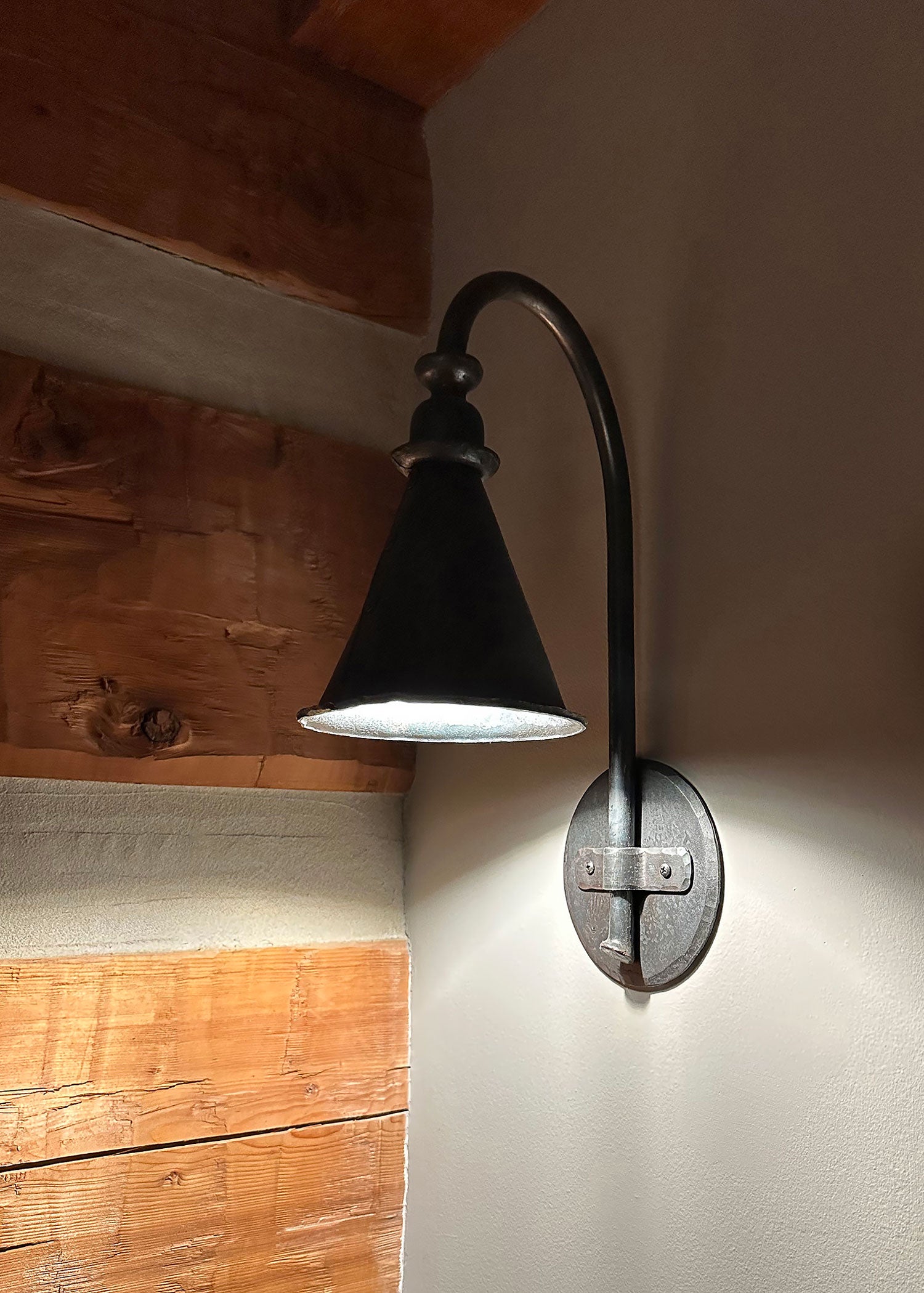 Hand forged wrought iron entry sconce with pendant style shade, tall gooseneck arm, and round backplate for exterior entry lighting.