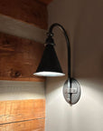Hand forged wrought iron entry sconce with pendant style shade, tall gooseneck arm, and round backplate for exterior entry lighting.