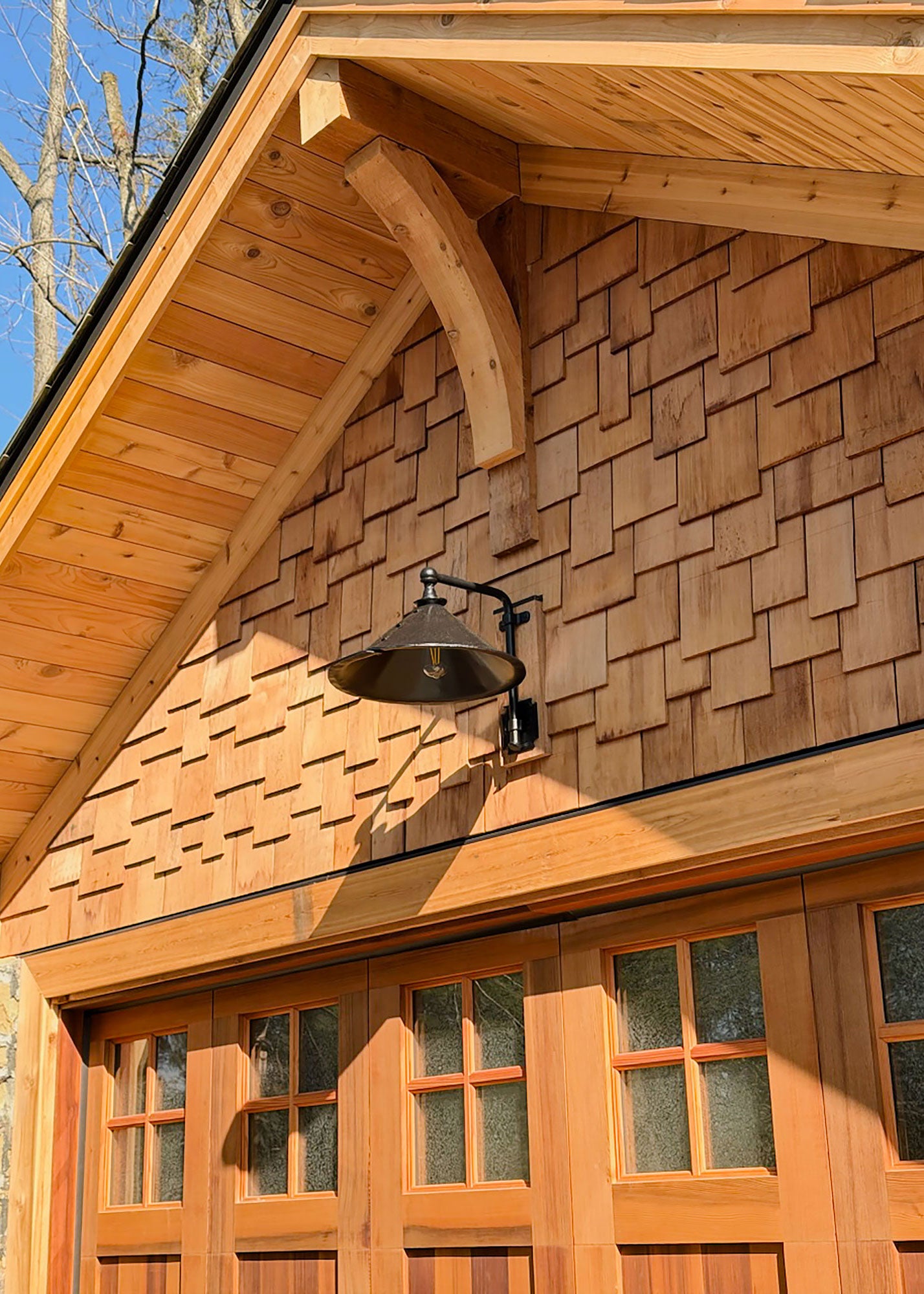 Hand forged wrought iron Estate Iron Wall Sconce mounted above a cedar garage door, showcasing rustic industrial barn style exterior lighting.