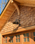 Hand forged wrought iron Estate Iron Wall Sconce mounted above a cedar garage door, showcasing rustic industrial barn style exterior lighting.