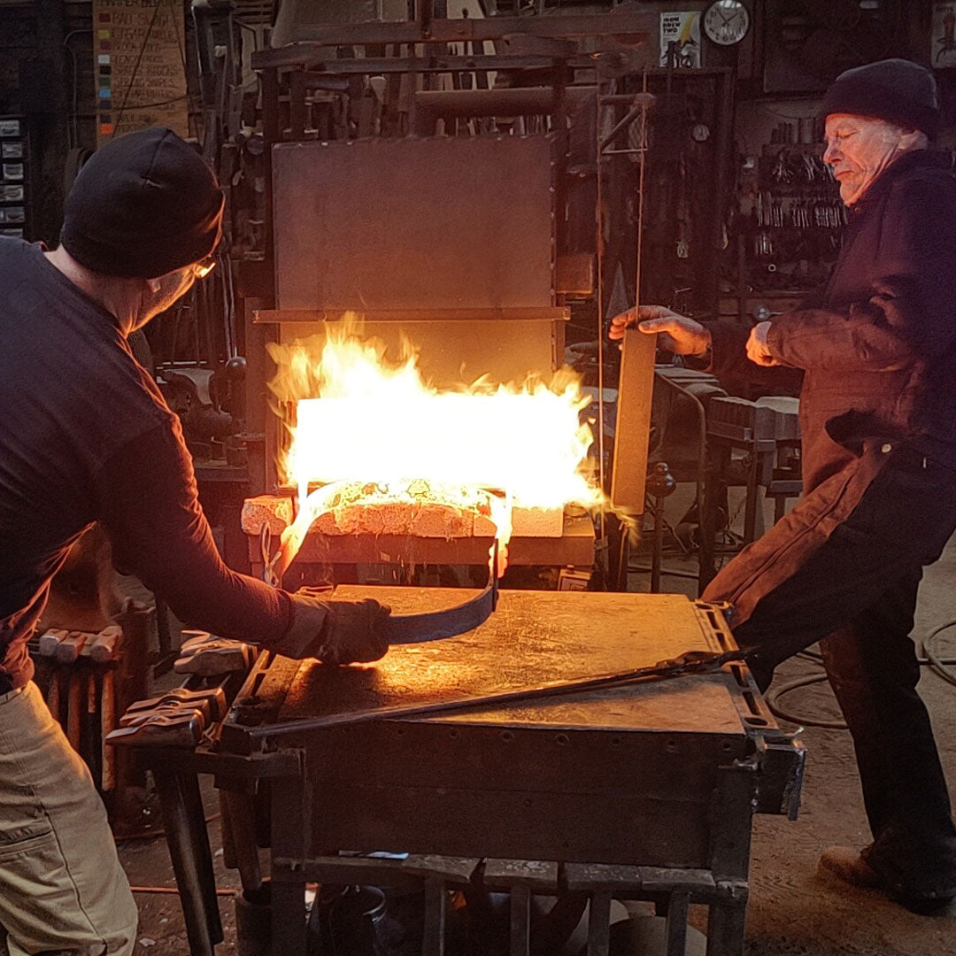Two men working with a forge in a workshop setting at Christopher Thomson Ironworks.