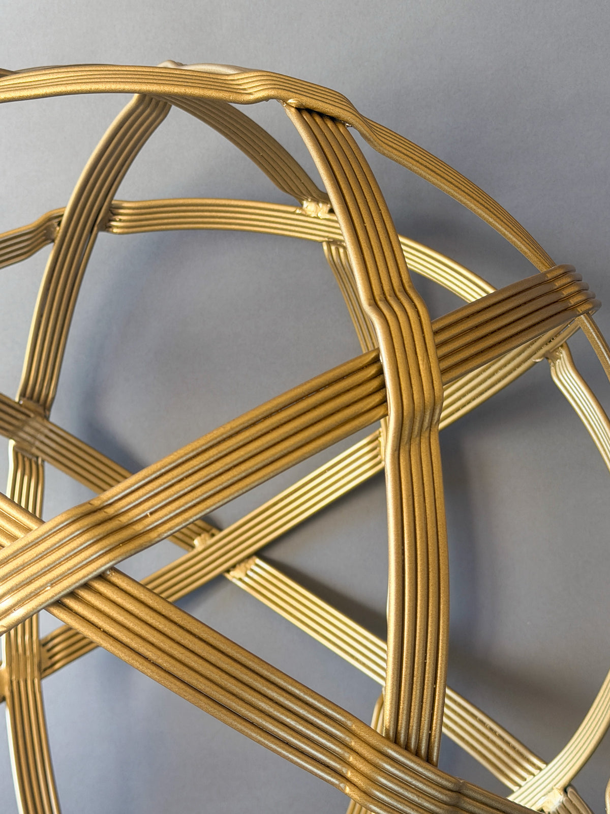 Close-up of gold powder-coated steel strands bending over and under where two bands cross