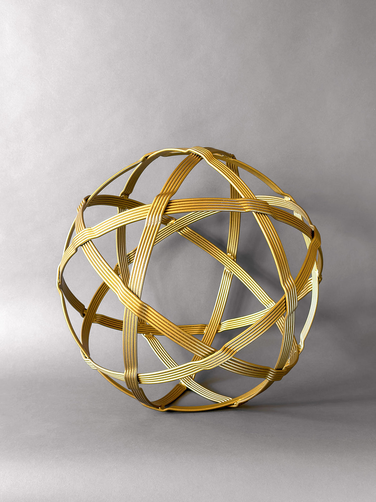 Front view of a 19-inch gold steel orb sculpture showing six woven bands framing triangles and pentagons