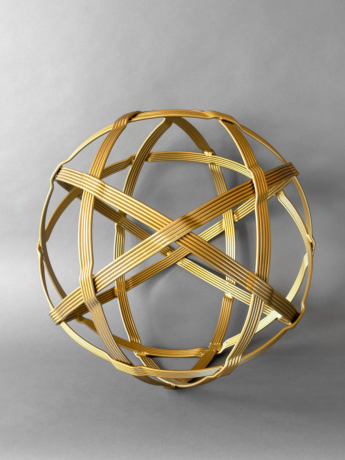 Gold Baby Chinlone orb sculpture, 19 inches, its bundled steel bands woven into an open sphere on a gray backdrop